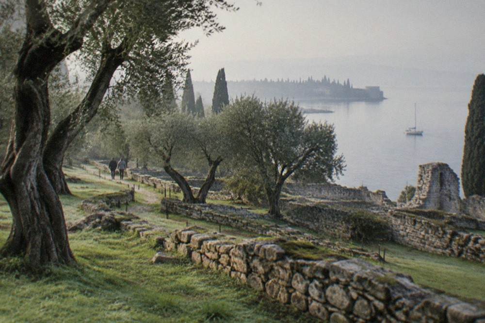 Low stone walls and olive trees of a Roman villa site above the shoreline of Lake Garda