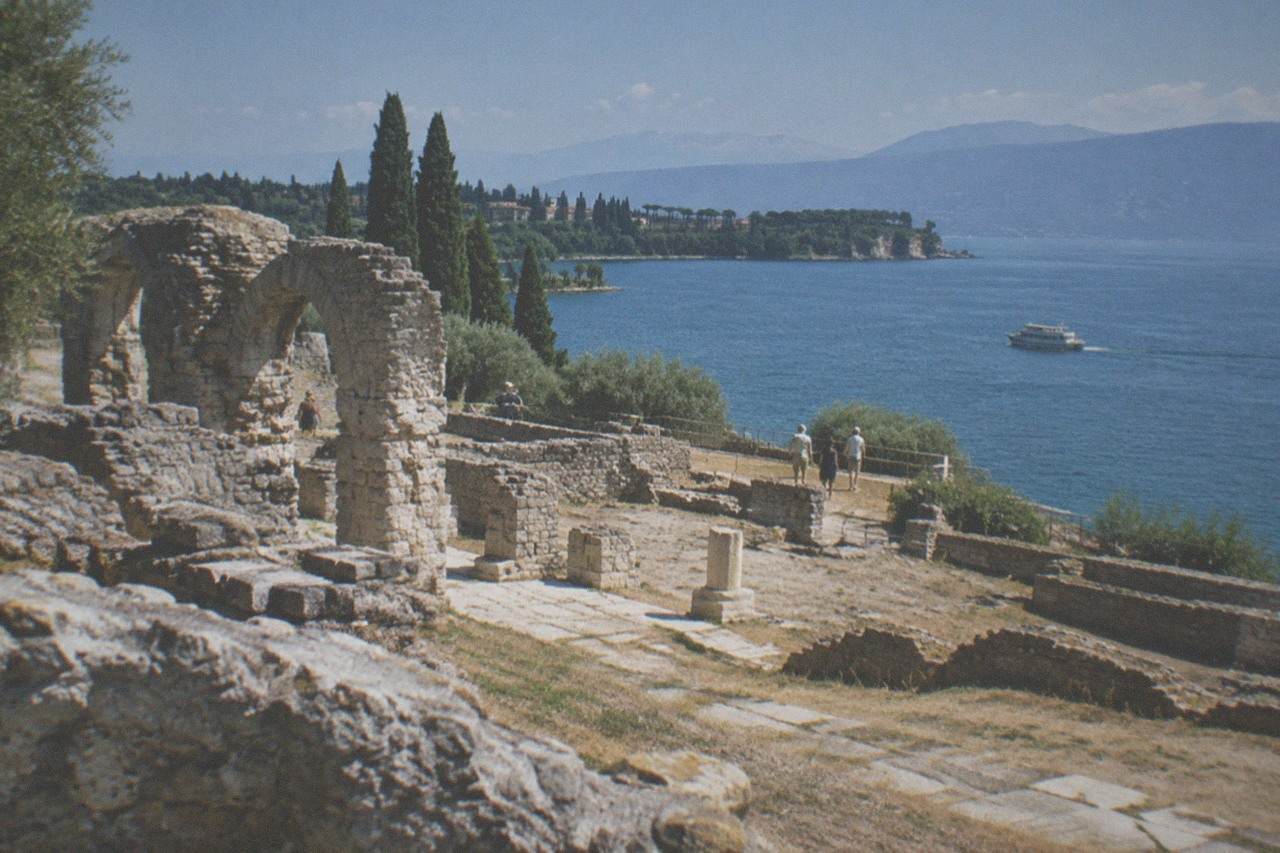Stone Roman ruins on a green headland above the blue water of Lake Garda