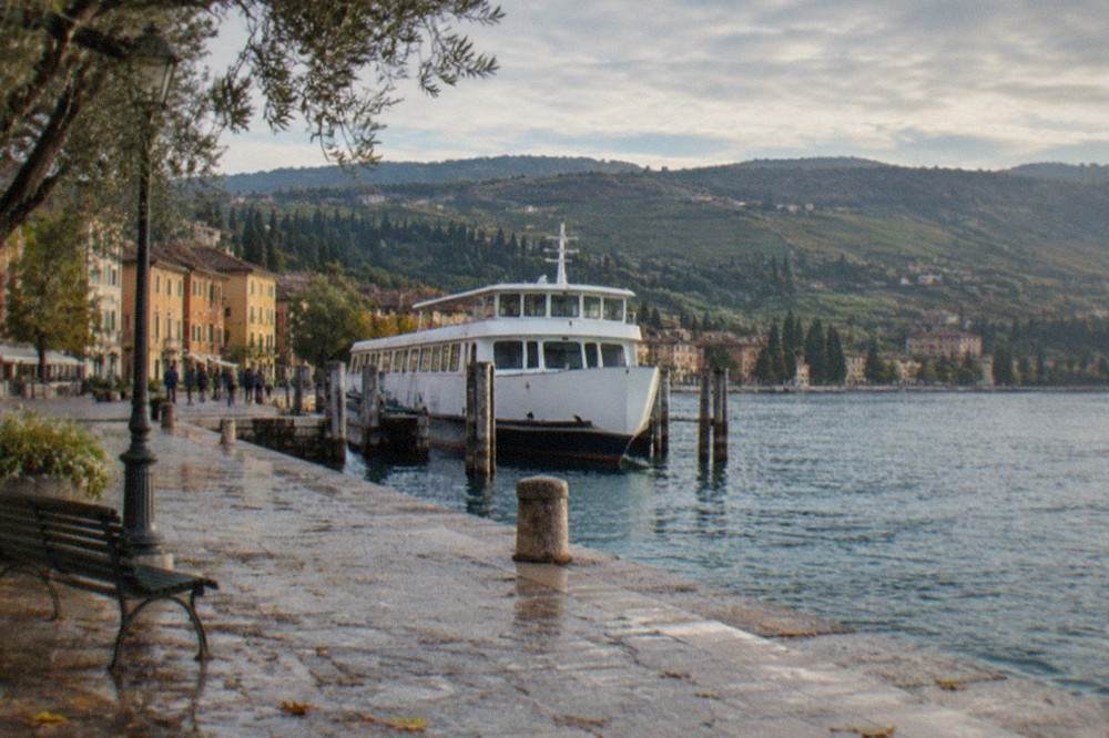 A white passenger ferry moored at a small lakeside pier with hills behind