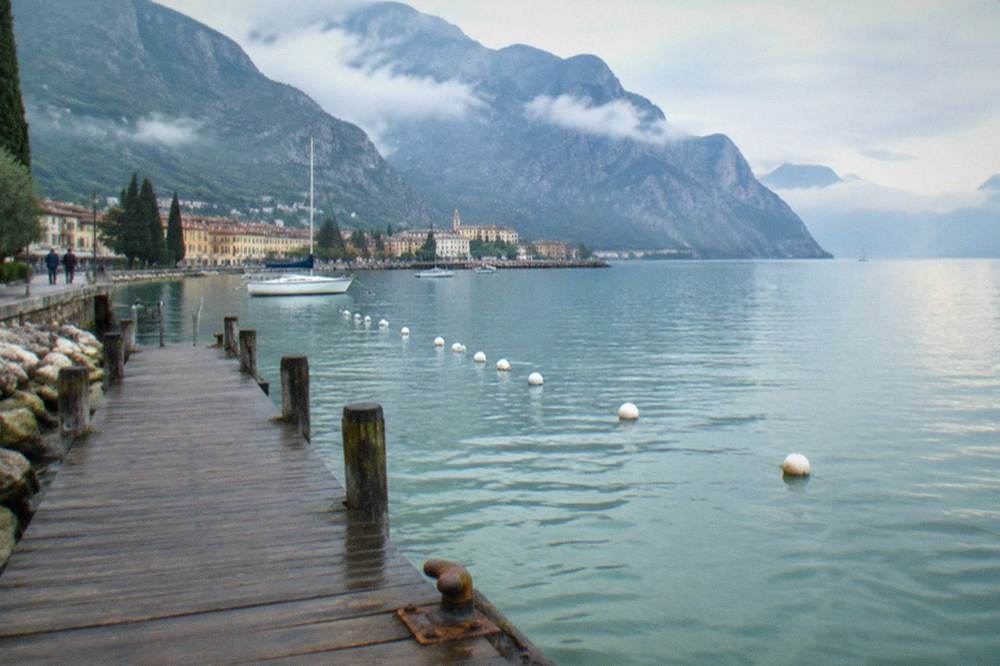 A wooden jetty on a rocky shoreline with buoys marking a swimming area on clear water