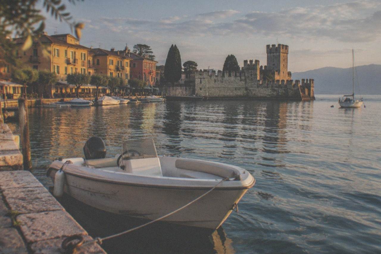 A small open motorboat moored at a stone jetty on a calm lake with a walled town behind it