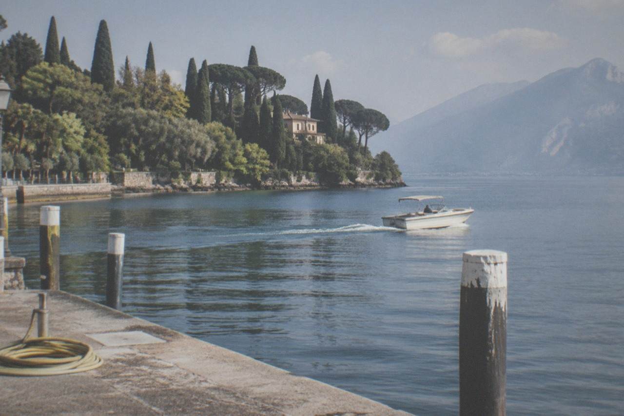 A small motorboat cruising on calm Lake Garda water near a wooded peninsula