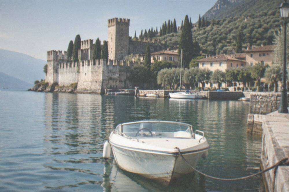 A small speedboat moored at a lakeside pier in front of a historic walled town