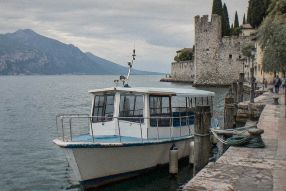 A passenger shuttle boat moored at a stone landing stage on the northern shore of Lake Garda