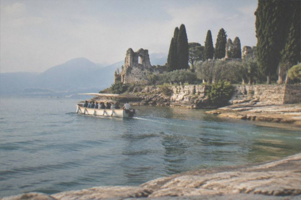 A small open tour boat cruising close to a rocky peninsula with a large Roman ruin on the headland