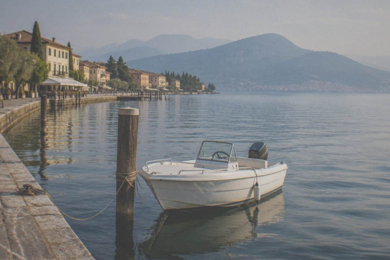 A small motorboat moored on calm water beside a stone lakefront with hills in the distance