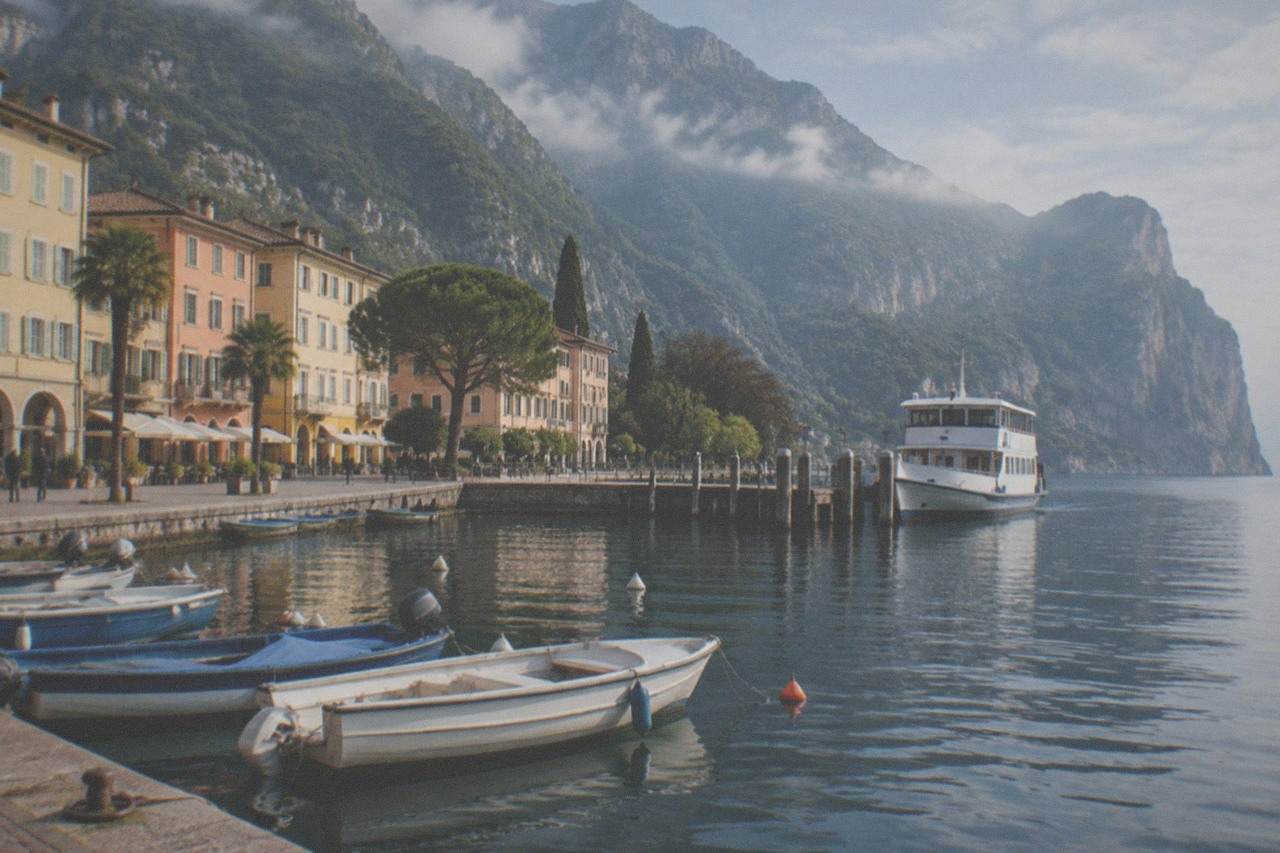 The harbour of Riva del Garda with moored boats, the old town waterfront and steep green mountains rising behind the lake.