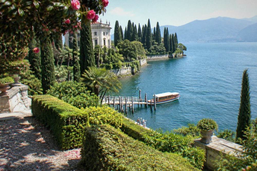 View from the island's upper terrace showing the formal gardens descending toward the lake with the boat pier visible