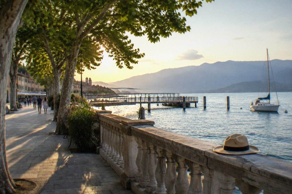 A wide lakeside promenade with trees and distant mountains across the water