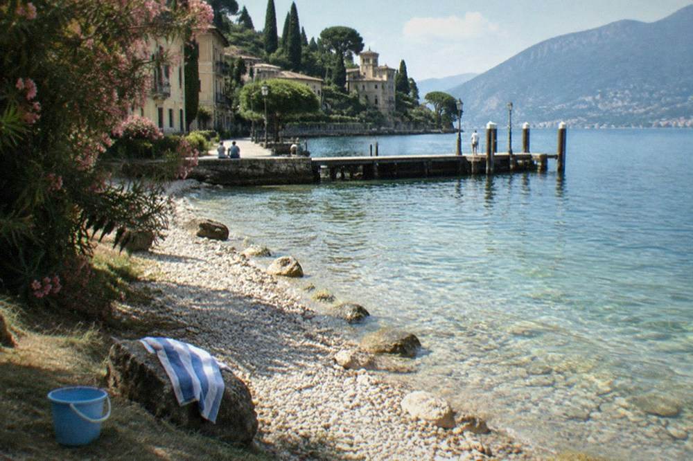 A shallow gravel beach on Lake Garda with clear water and a shaded grassy edge