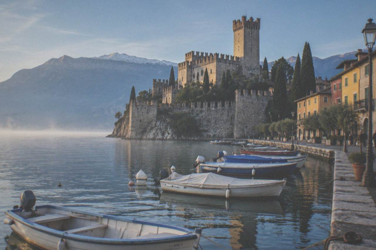 The harbour and stone towers of Malcesine at the edge of Lake Garda beneath a mountain ridge