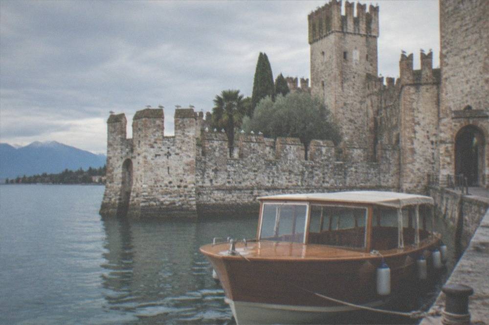 A wooden tour boat moored at a stone jetty in the small harbour inside the walls of Sirmione