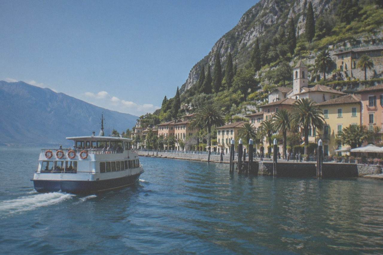 A passenger ferry crossing open water toward a lakeside town with hills behind it