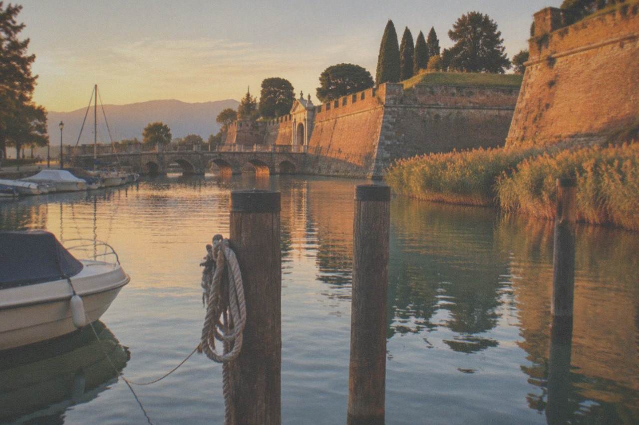 Wooden mooring posts in still water with a lakeside town and mountains beyond at golden hour