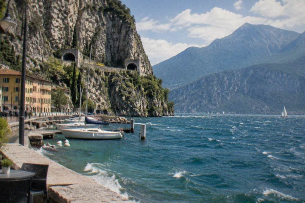 A cliff road with tunnels hugging a rocky slope above deep blue lake water