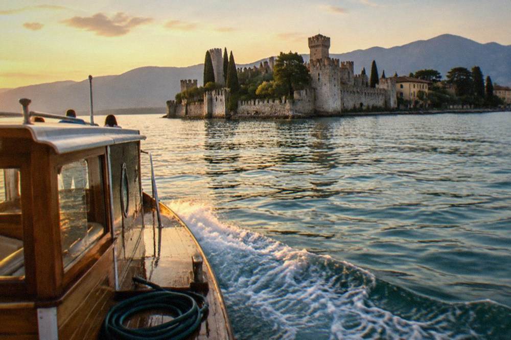A small wooden tour boat crossing open water toward a walled peninsula town at golden hour