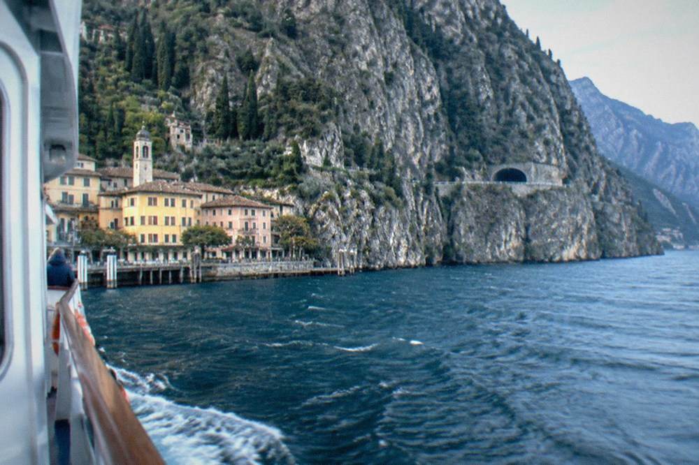 A cliff coastline above deep lake water with a road tunnel visible in the rock