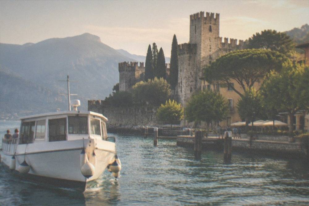 A passenger boat approaching a lakeside town with a stone castle above the harbour