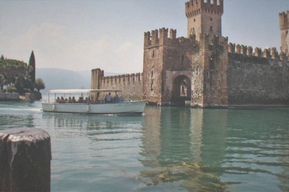 Tour boat cruising past the fortified harbour walls and castle of Sirmione on Lake Garda