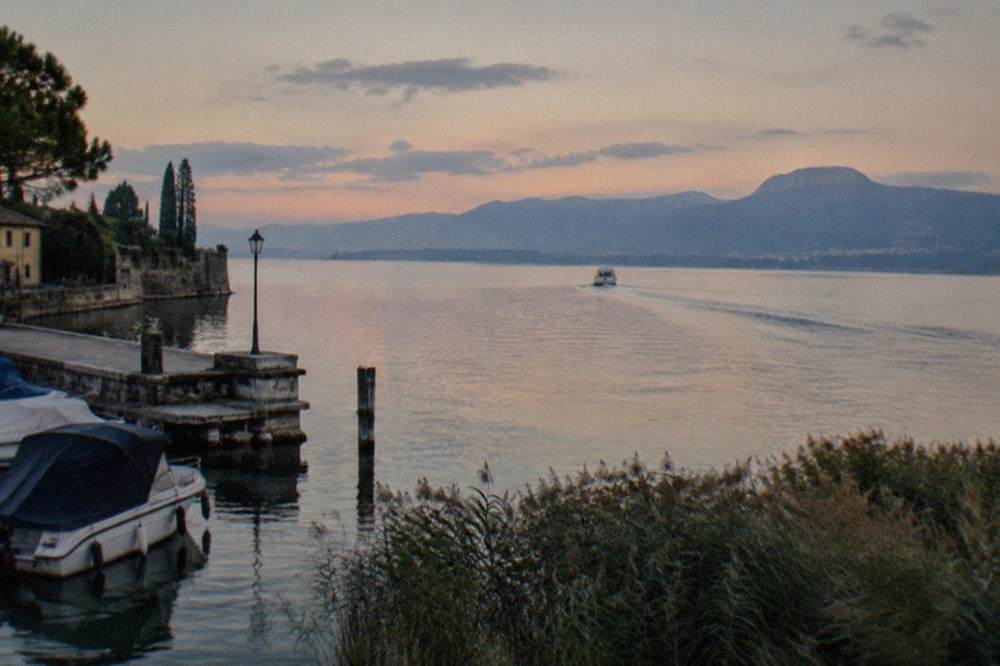 Wide view across the southern basin of Lake Garda with a small boat leaving a wake