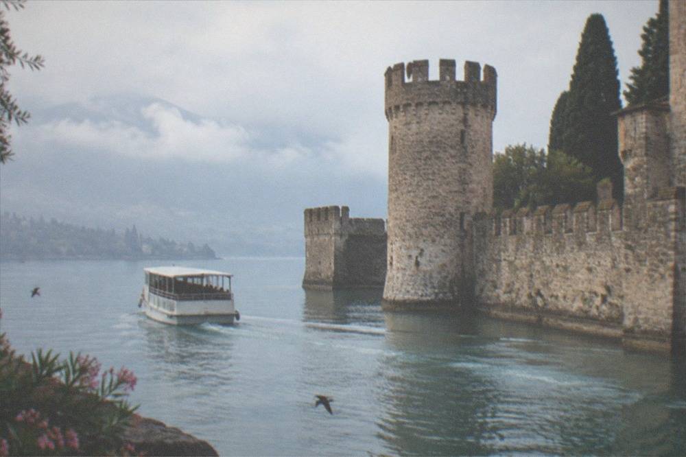 A tour boat passing the fortified walls and tower of a lakeside castle town