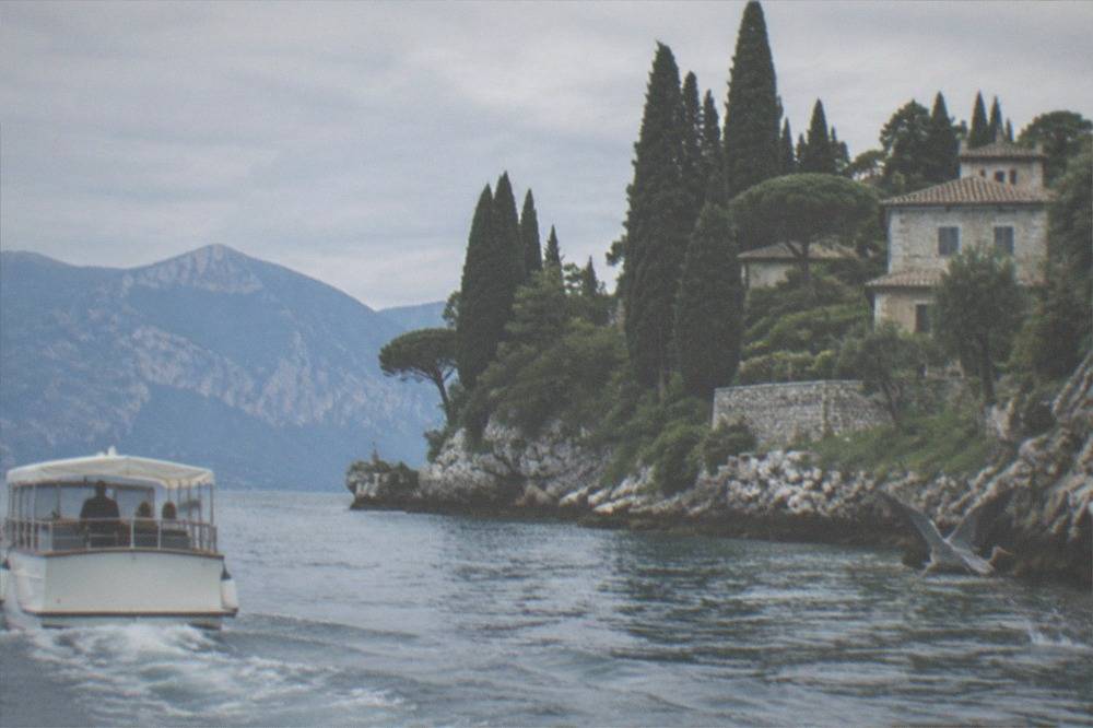 A skippered cruise boat on Lake Garda passing a rocky headland with cypress trees