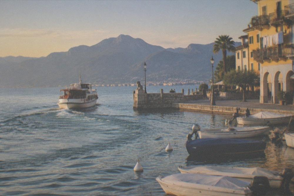 A small cruise boat departing Desenzano harbour in late afternoon light