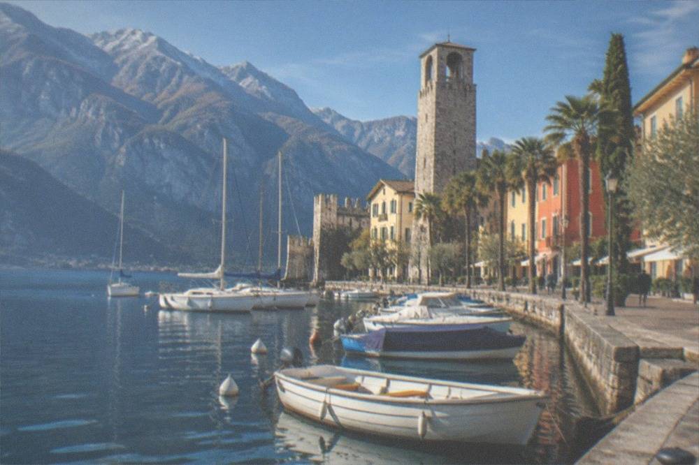 A lakeside promenade with a stone tower and boats moored along the water's edge