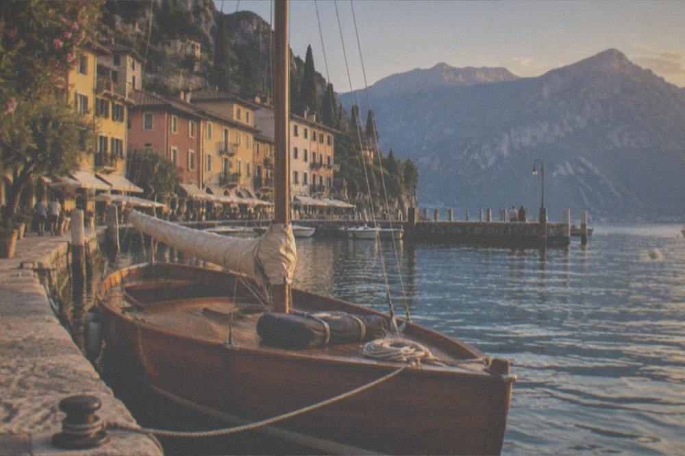A wooden sailing boat moored in a small harbour at golden hour with mountains behind