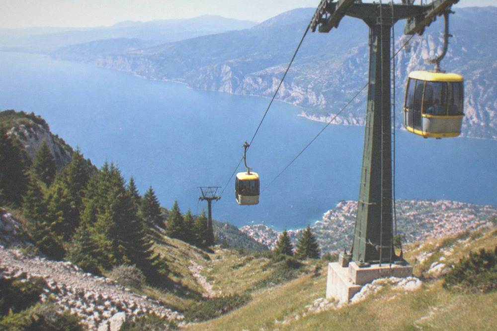 Cable car cabins ascending a steep mountain slope above Malcesine and the blue expanse of the lake