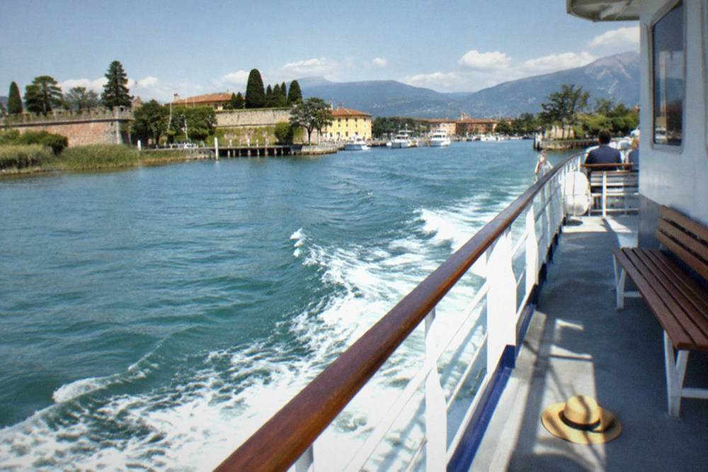 A passenger boat crossing the open water of southern Lake Garda toward the Sirmione peninsula