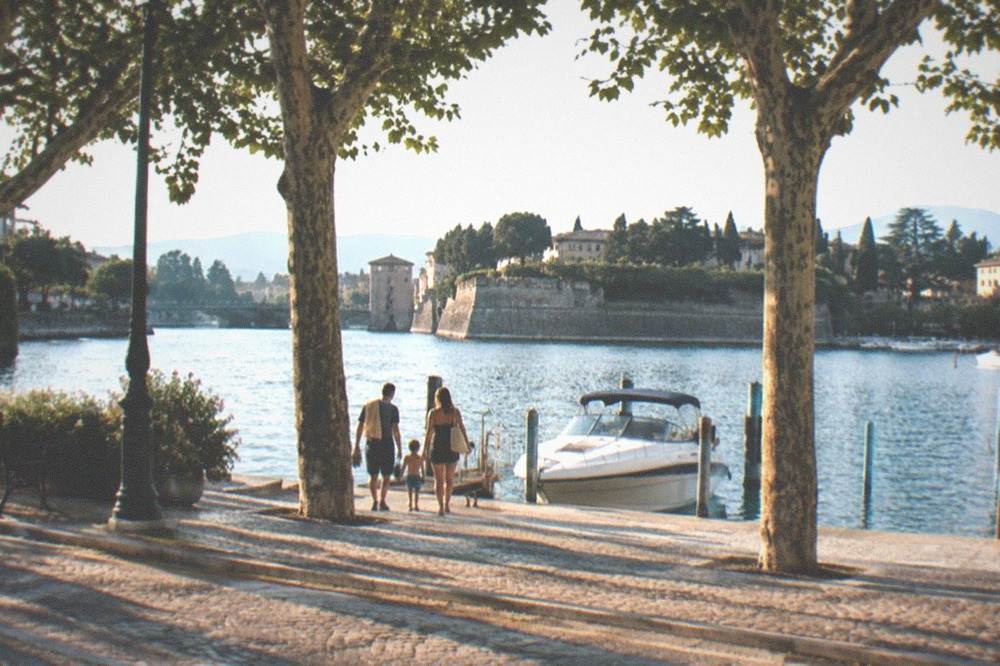 A family walking from the Peschiera lakefront toward the boats at the landing in late afternoon light