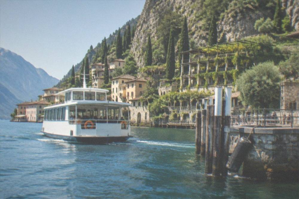 A white ferry approaching a stone landing stage on the western shore of Lake Garda
