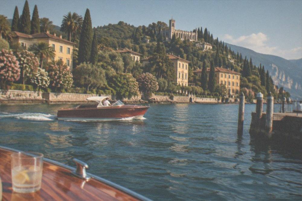 A varnished wooden motor boat cruising along a shoreline of trees and villas