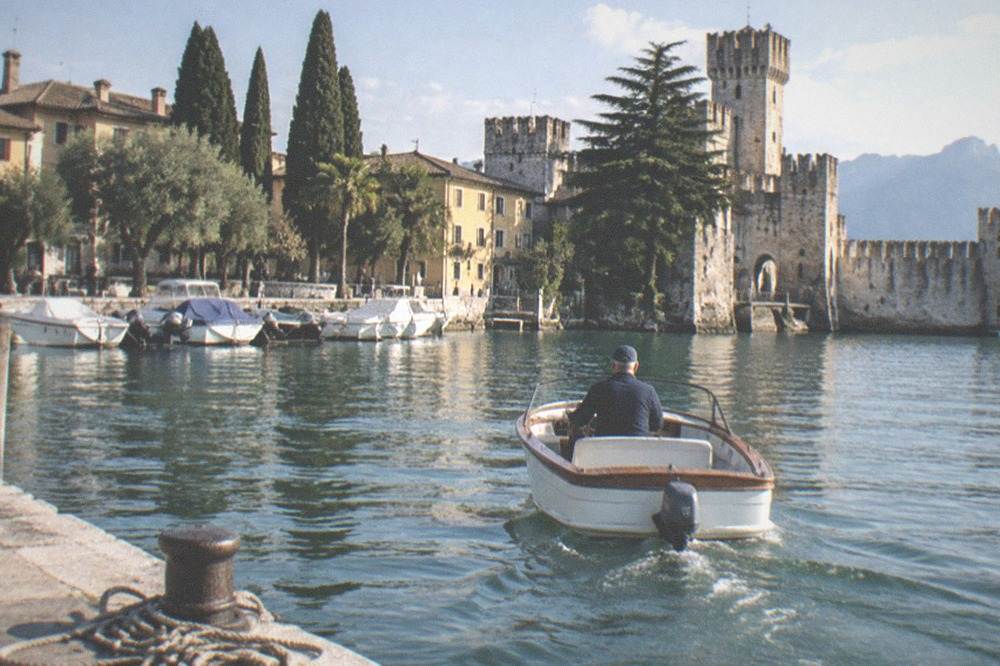 A small private boat with a skipper at the helm leaving Sirmione harbour in late afternoon light