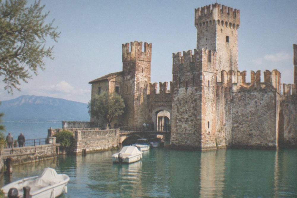 A stone castle tower rising above a small harbour with boats and a long peninsula stretching into blue water