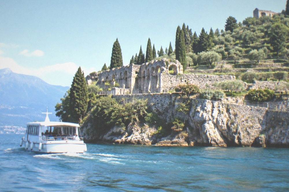 A small passenger boat cruising past rocky cliffs above clear water along a peninsula shoreline