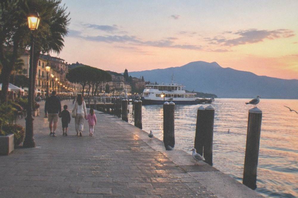 Families walking along a lakefront promenade toward a boat landing in the evening light