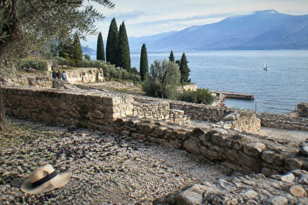 Low Roman walls and terraces of an excavated villa site with olive trees and lake beyond
