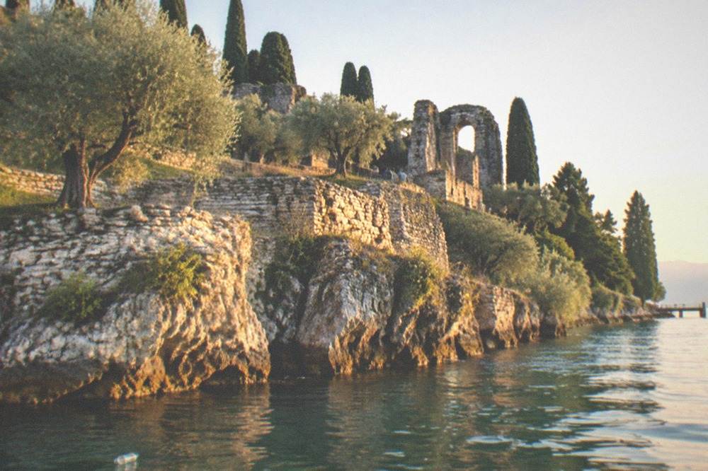 A lake headland at golden hour with stone terraces and olive trees above still water