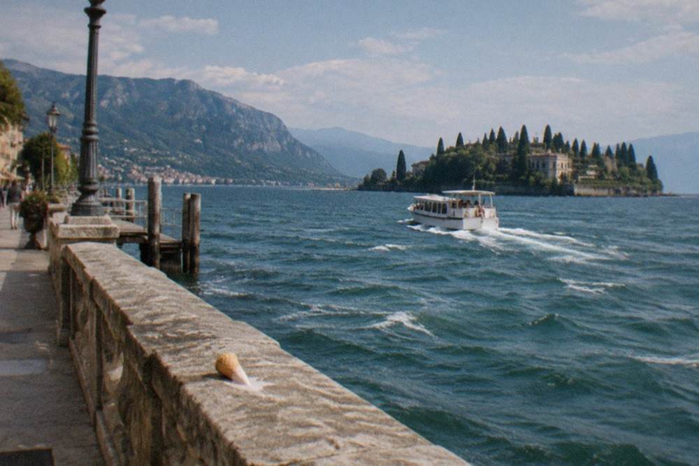 A small passenger boat approaching a terraced island shore with cypress trees