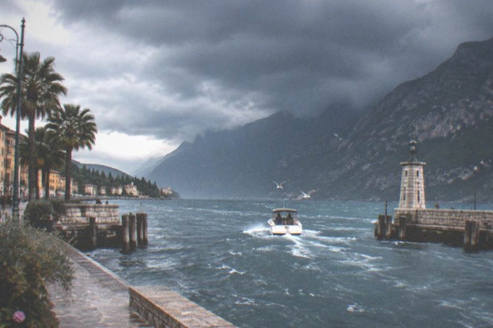Dark clouds gathering over a Lake Garda bay with a small boat heading toward a sheltered harbour