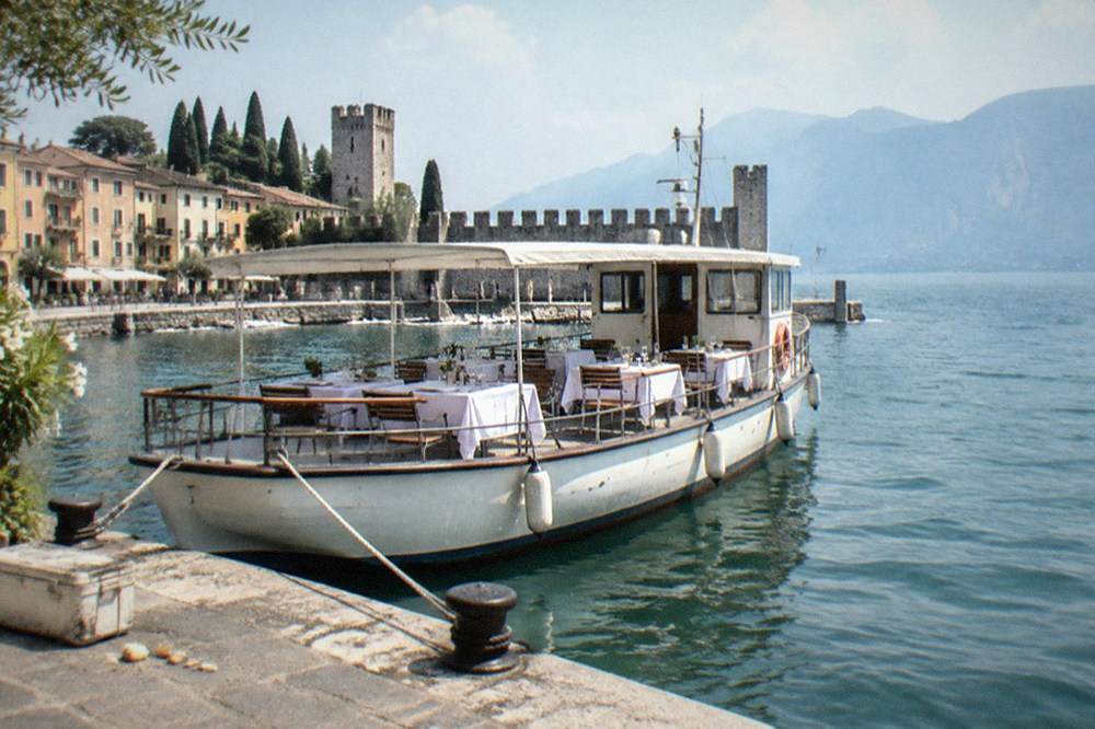A passenger cruise boat moored at a Lake Garda town quay with tables set for lunch on deck