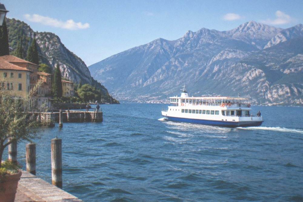 A large public ferry crossing the open water of Lake Garda with mountains rising behind it