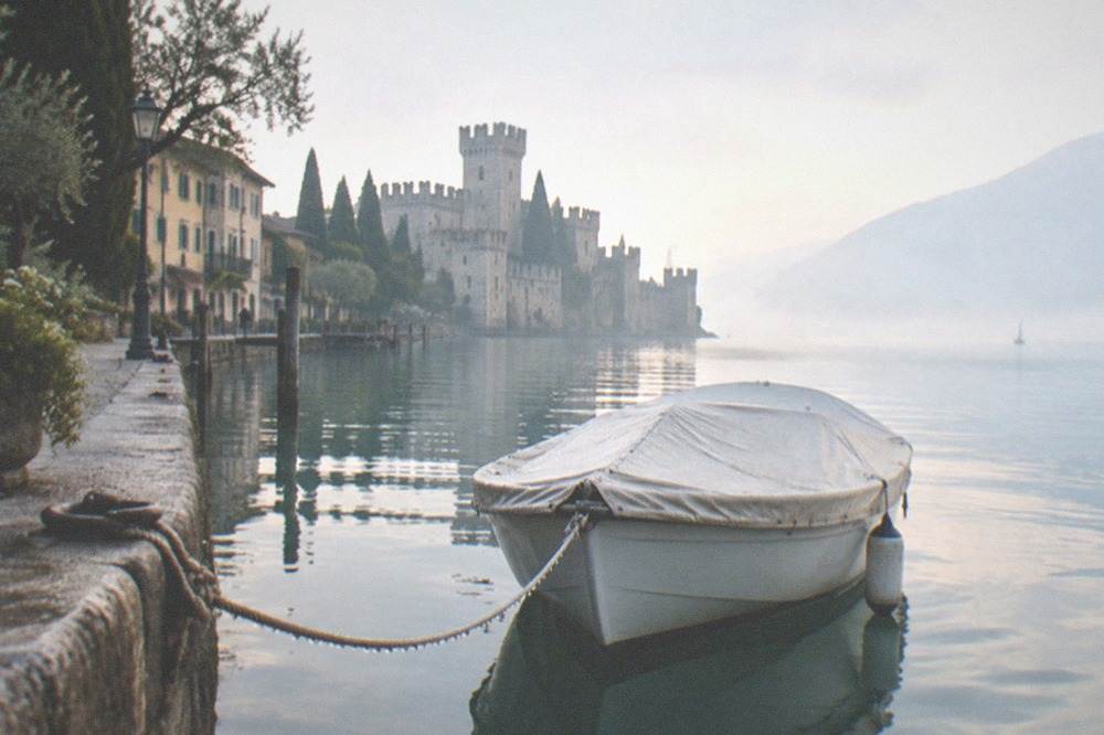 A small covered boat moored on flat early morning water beside a stone pier