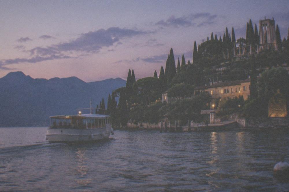 A tour boat crossing calm water towards a lakeside town in early evening light