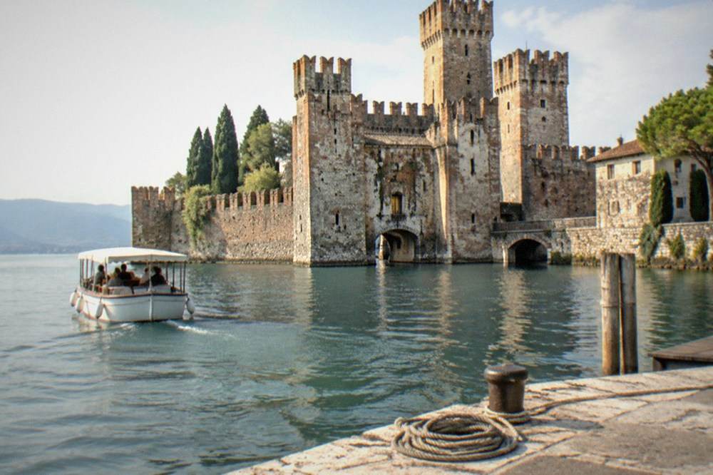 A small boat departing from the dock at Sirmione with the Scaligero Castle in the background