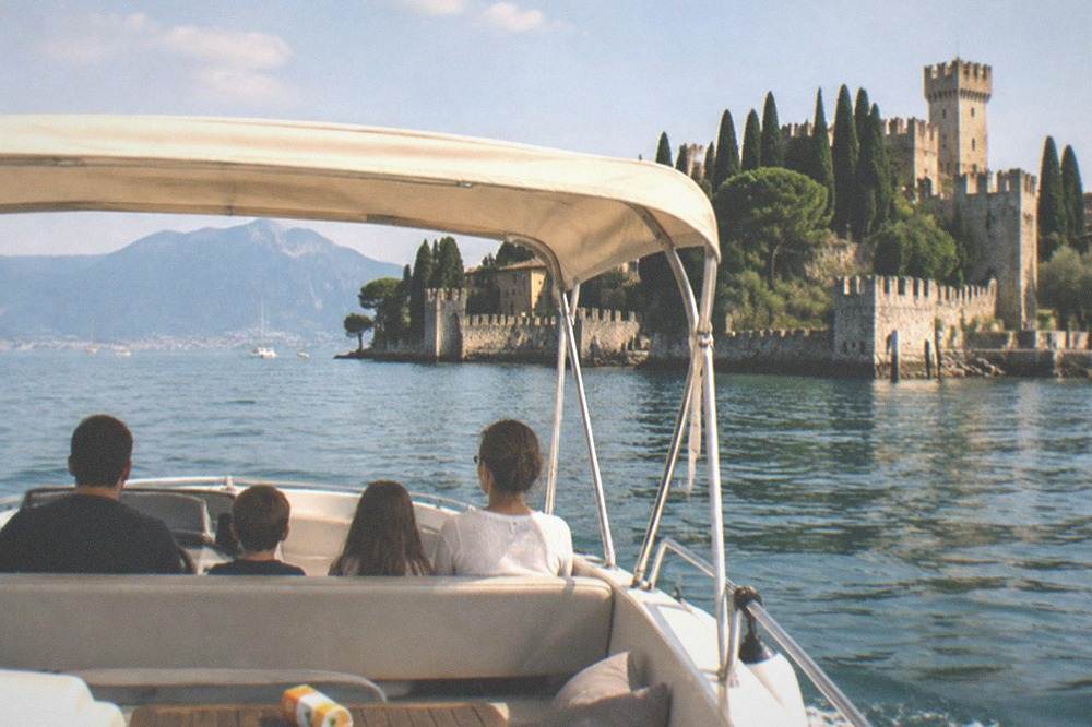 A private boat with a bimini top and a family of four seated comfortably, with the Sirmione peninsula in the background