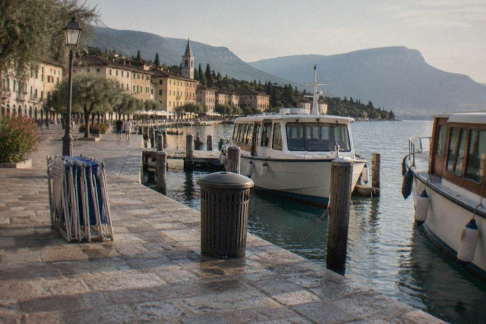 A lakeside promenade with a stone pier and moored passenger boats in the morning light