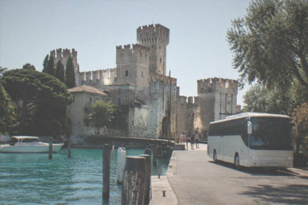 A coach parked near the Sirmione waterfront with the castle towers behind